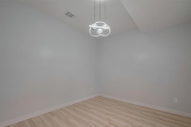 spare room with a chandelier, light wood finished floors, and baseboards