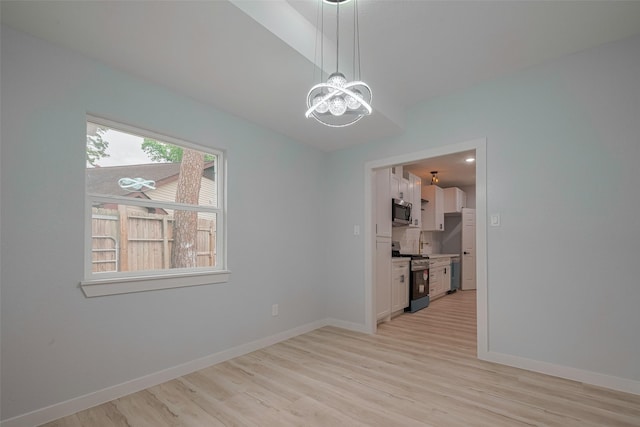 spare room with a chandelier, light wood-style floors, and baseboards