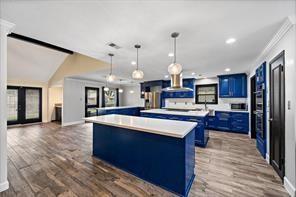 15418 Windy Cove Dr, Houston, TX 77095 - kitchen featuring blue cabinets, a center island, ornamental molding, light countertops, and dark wood finished floors
