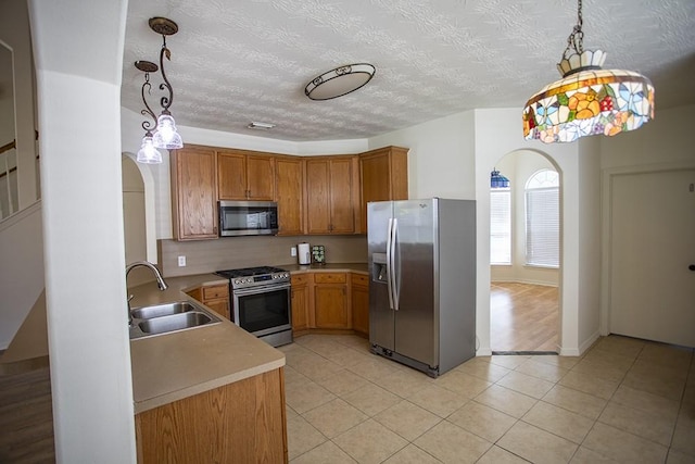 21926 Crestworth Ln, Katy, TX 77449 - kitchen featuring appliances with stainless steel finishes, a sink, arched walkways, light countertops, and brown cabinetry
