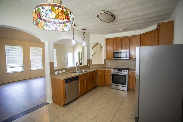 21926 Crestworth Ln, Katy, TX 77449 - kitchen featuring appliances with stainless steel finishes, a sink, light tile patterned flooring, brown cabinets, and a textured ceiling