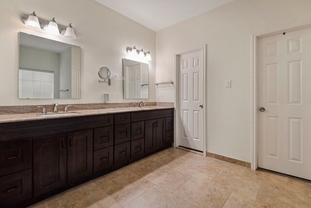 full bath with baseboards, stone tile floors, and double vanity