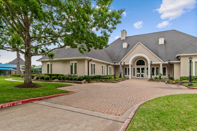 view of front facade with curved driveway, stucco siding, a chimney, french doors, and a front yard