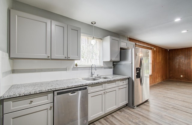 9502 Kell Cir, Houston, TX 77040 - kitchen featuring appliances with stainless steel finishes, a sink, light wood finished floors, wooden walls, and pendant lighting