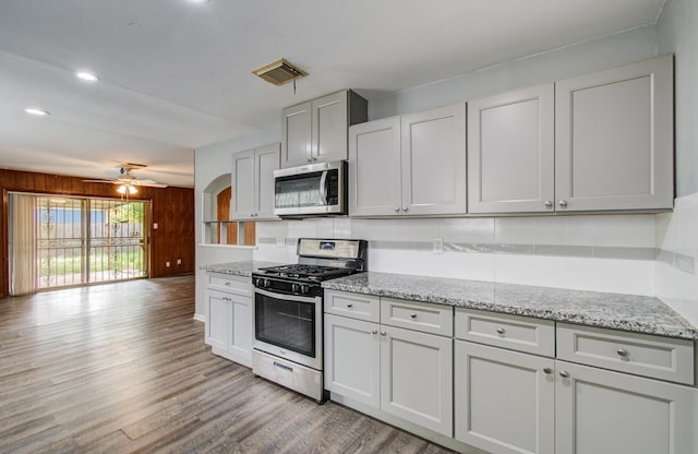 9502 Kell Cir, Houston, TX 77040 - kitchen featuring appliances with stainless steel finishes, light wood-style floors, light stone counters, a ceiling fan, and wood walls
