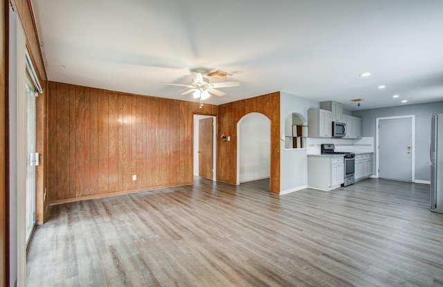 9502 Kell Cir, Houston, TX 77040 - unfurnished living room featuring ceiling fan, light wood-style floors, wood walls, arched walkways, and baseboards