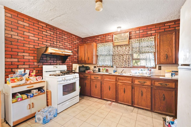 2316 Cleveland Ave, Waco, TX 76706 - kitchen featuring white range with gas cooktop, under cabinet range hood, a textured ceiling, light tile patterned floors, and brick wall