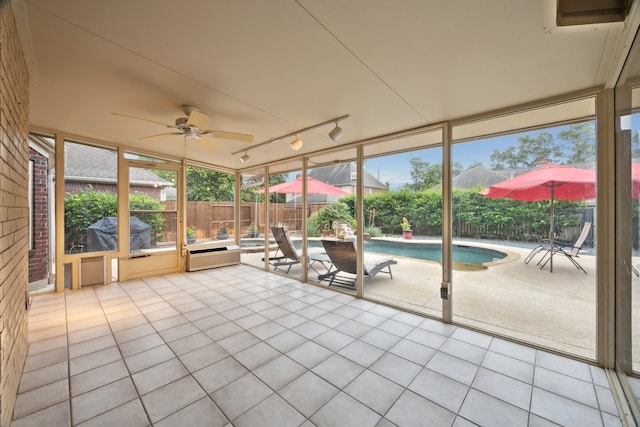 unfurnished sunroom featuring rail lighting, a ceiling fan, and plenty of natural light