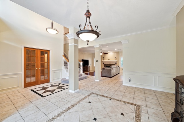 entrance foyer featuring decorative columns, a decorative wall, french doors, a tile fireplace, and stairway