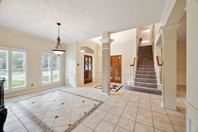 entryway with a decorative wall, decorative columns, inlaid floor details, ornamental molding, and stairway
