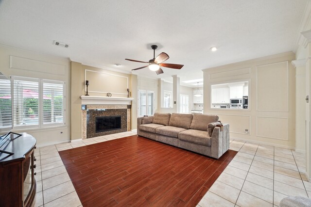 living area featuring crown molding, a ceiling fan, a decorative wall, a high end fireplace, and wood finished floors