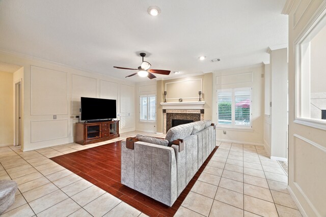 living area featuring ornamental molding, a fireplace, ceiling fan, light tile patterned floors, and baseboards