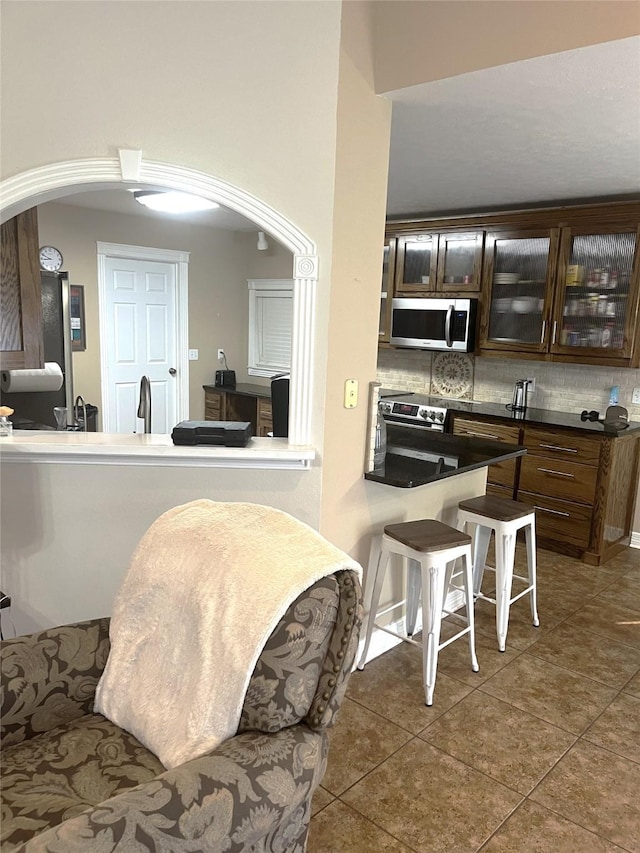 202 Golfview Dr, Normangee, TX 77871 - kitchen with appliances with stainless steel finishes, arched walkways, tile patterned flooring, glass insert cabinets, and backsplash