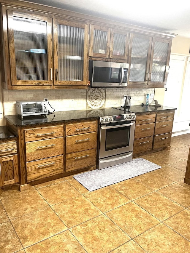202 Golfview Dr, Normangee, TX 77871 - kitchen featuring appliances with stainless steel finishes, decorative backsplash, brown cabinetry, and glass insert cabinets