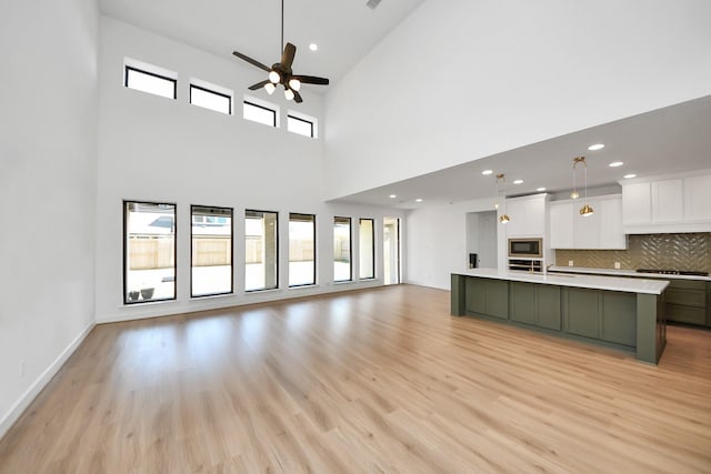 unfurnished living room with healthy amount of natural light, light wood-type flooring, a ceiling fan, recessed lighting, and a high ceiling