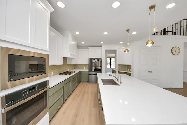 kitchen featuring stainless steel appliances, a sink, white cabinets, decorative backsplash, and light countertops