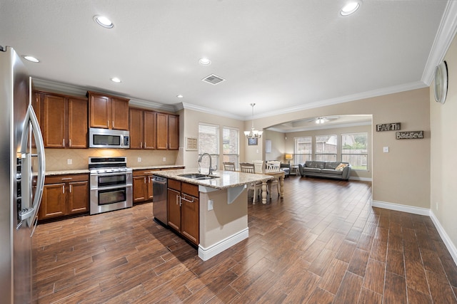kitchen with stainless steel appliances, a sink, brown cabinetry, open floor plan, and tasteful backsplash