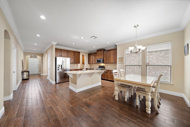 kitchen with stainless steel appliances, a sink, brown cabinets, a kitchen bar, and arched walkways