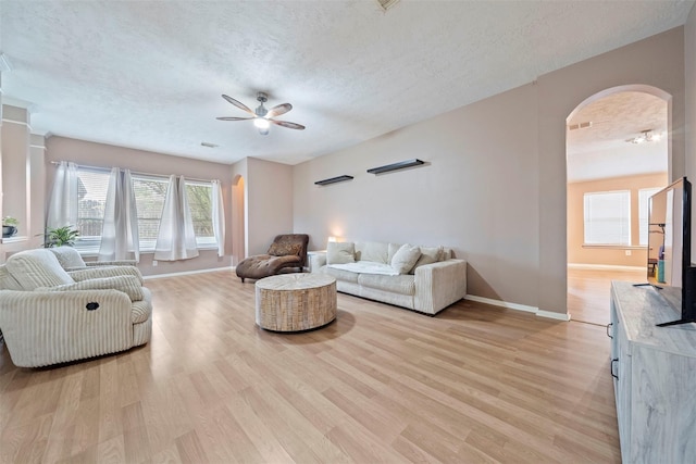 living area with arched walkways, a ceiling fan, a textured ceiling, light wood finished floors, and baseboards