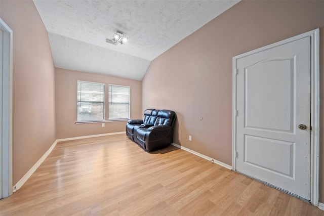 unfurnished room with a textured ceiling, vaulted ceiling, light wood-style floors, and baseboards