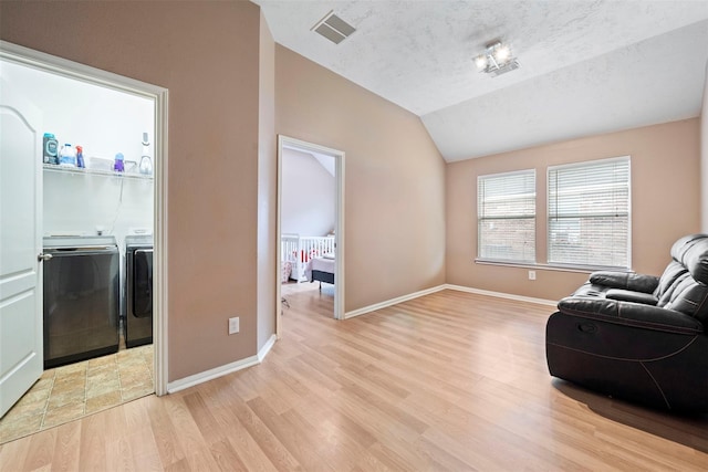 living area featuring independent washer and dryer, lofted ceiling, light wood finished floors, baseboards, and a textured ceiling