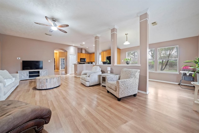 living room with light wood-style floors, ceiling fan, arched walkways, and baseboards