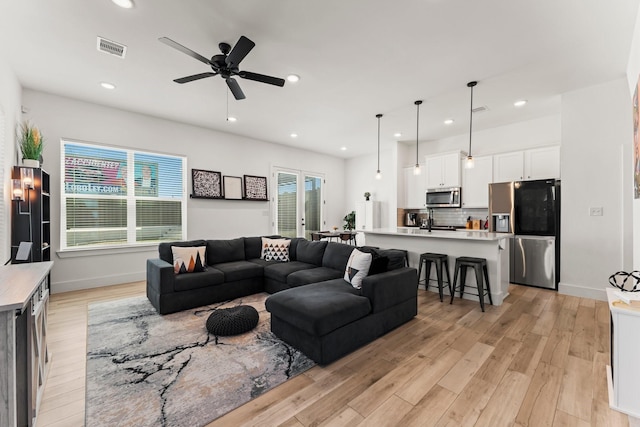 living room with light wood-type flooring, a ceiling fan, recessed lighting, and baseboards