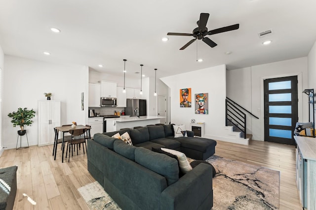 living area with stairway, light wood-style flooring, ceiling fan, and recessed lighting