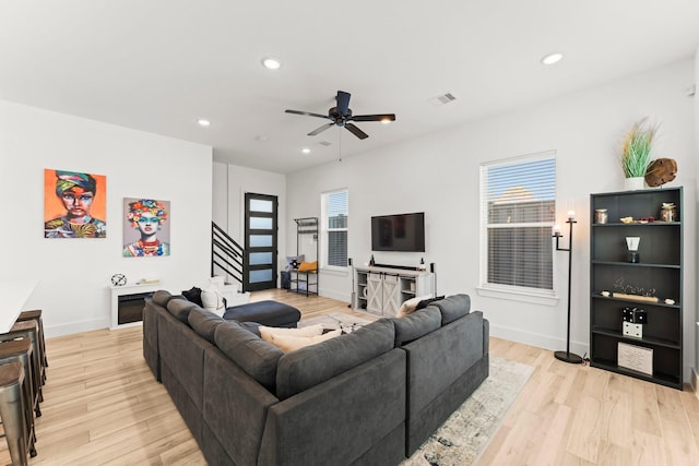 living room featuring light wood-style floors, a ceiling fan, healthy amount of natural light, stairs, and recessed lighting