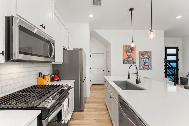 kitchen featuring appliances with stainless steel finishes, a sink, light wood-style flooring, tasteful backsplash, and white cabinetry