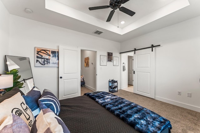 carpeted bedroom featuring a barn door, a tray ceiling, baseboards, recessed lighting, and a ceiling fan