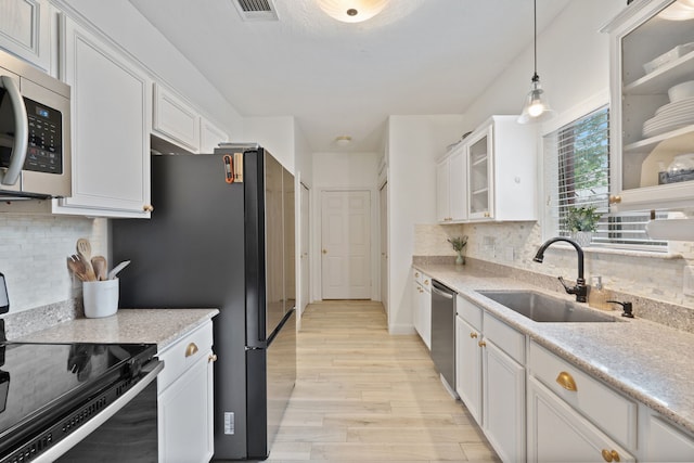 2838 Sunburst Ln, Montgomery, TX 77356 - kitchen with appliances with stainless steel finishes, a sink, white cabinets, light wood finished floors, and decorative backsplash