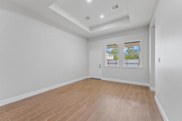 empty room featuring a raised ceiling, light wood finished floors, baseboards, and recessed lighting