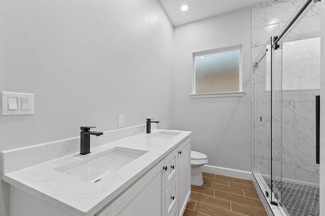 full bath featuring a marble finish shower, toilet, double vanity, wood finish floors, and baseboards