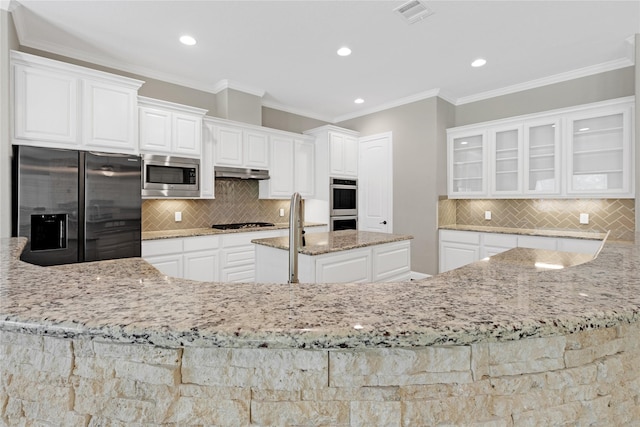 28116 Chuckwagon Trl, Magnolia, TX 77355 - kitchen featuring appliances with stainless steel finishes, under cabinet range hood, backsplash, light stone countertops, and white cabinetry