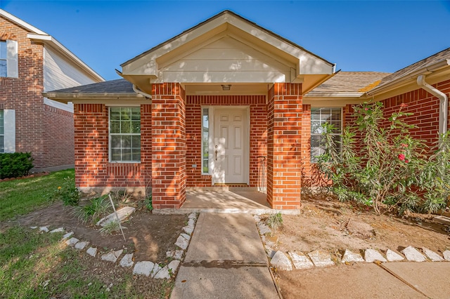 doorway to property with brick siding and a shingled roof