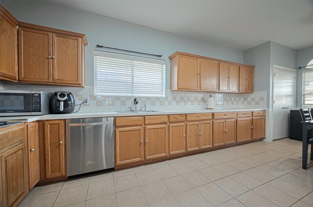 kitchen with appliances with stainless steel finishes, a sink, decorative backsplash, and light countertops