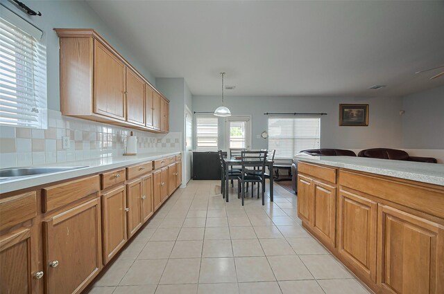 kitchen with light tile patterned flooring, light countertops, backsplash, brown cabinets, and pendant lighting