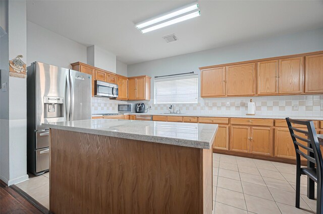 kitchen with stainless steel appliances, a sink, a kitchen island, backsplash, and light stone counters
