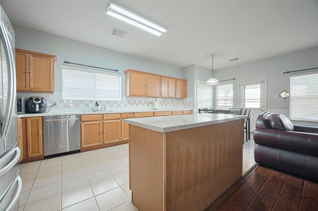 kitchen featuring stainless steel appliances, light countertops, backsplash, a kitchen island, and a sink