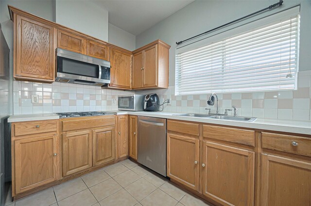 kitchen with appliances with stainless steel finishes, a sink, decorative backsplash, light tile patterned floors, and light countertops