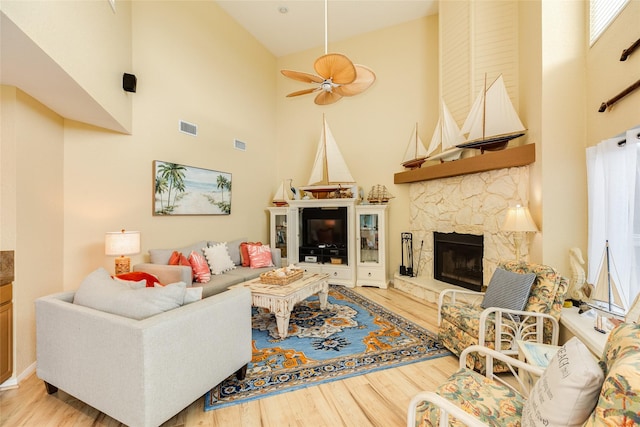 living room featuring a high ceiling, wood finished floors, a fireplace, and ceiling fan