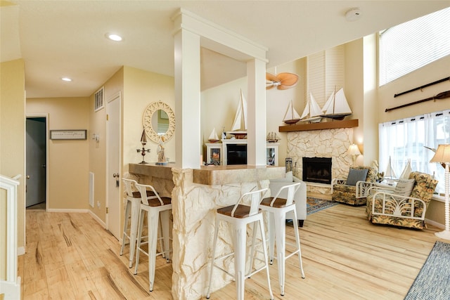 kitchen with wood finished floors, a stone fireplace, a breakfast bar, recessed lighting, and baseboards