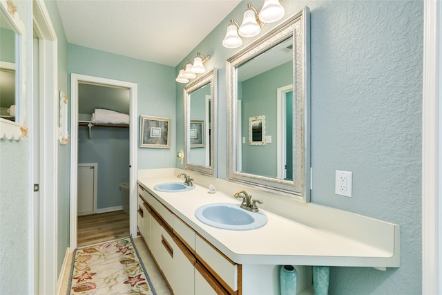 bathroom with wood finished floors, a textured wall, and double vanity