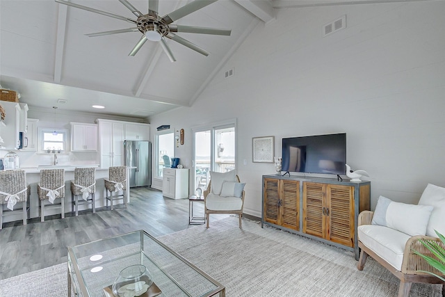 living area with light wood-style floors, beamed ceiling, high vaulted ceiling, and a ceiling fan
