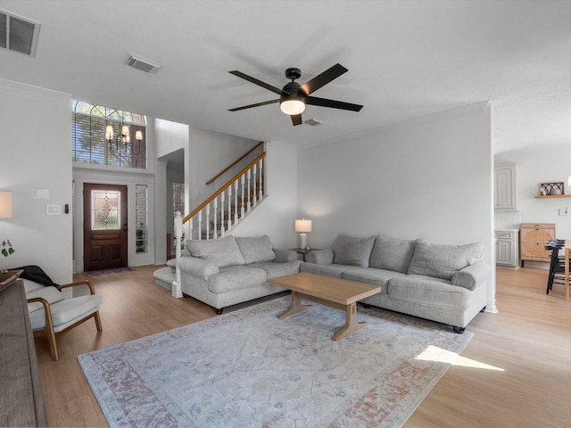 living room with light wood finished floors, a chandelier, a ceiling fan, stairway, and ornamental molding