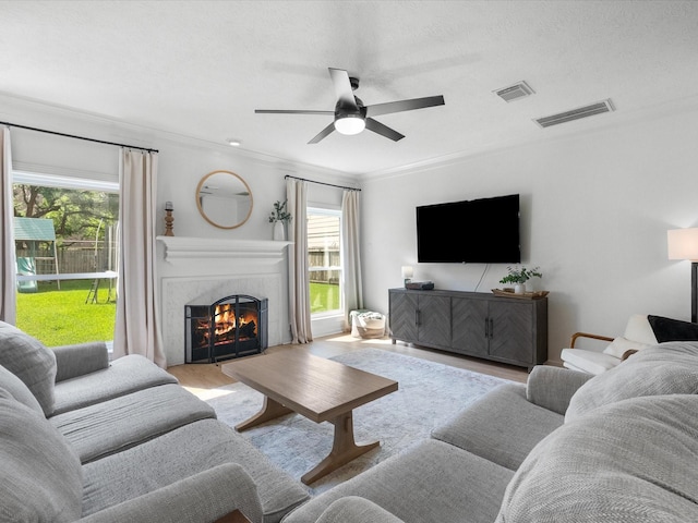 living room featuring a high end fireplace, plenty of natural light, ceiling fan, ornamental molding, and wood finished floors