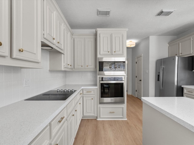 kitchen featuring appliances with stainless steel finishes, light countertops, light wood-type flooring, decorative backsplash, and a textured ceiling