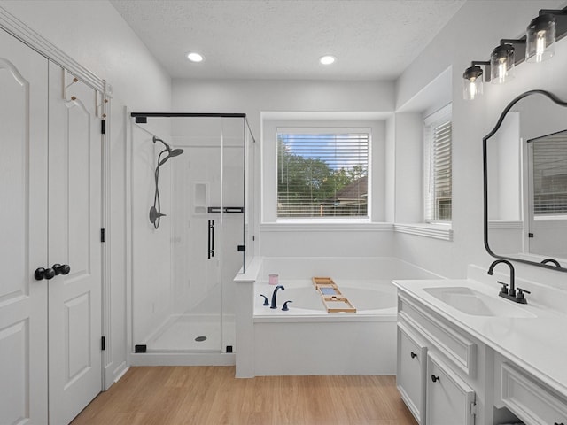 bathroom featuring a stall shower, vanity, a garden tub, a textured ceiling, and wood finished floors