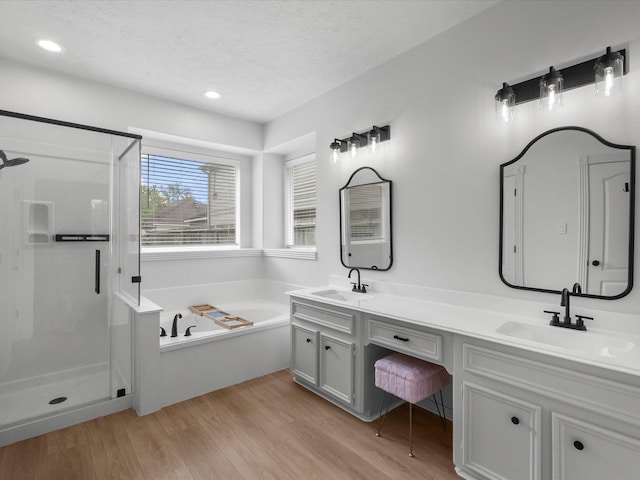 bathroom featuring a stall shower, double vanity, wood finished floors, a garden tub, and a textured ceiling